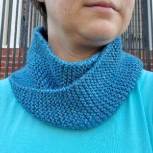 A pale person wearing a sky blue shirt and an aqua blue knitted infinity cowl